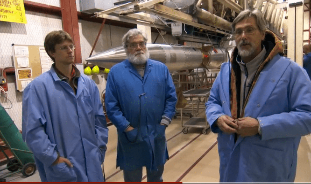 three people in lab coats standing in front of rockets