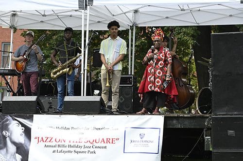 Woman in vibrant pattern speaking in front of band