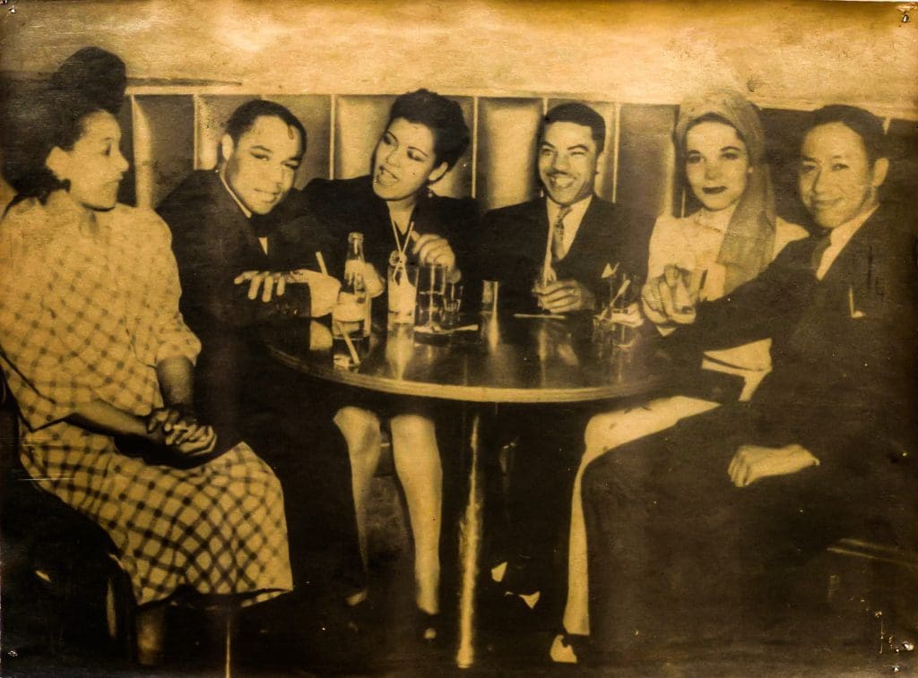 three women and six men laughing around a booth table in 1930s suits  and dresses