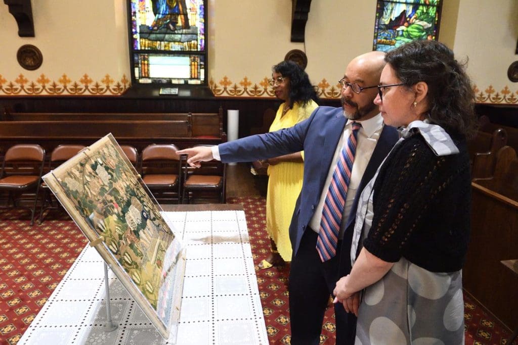 Dr. Jackson and two exhibition visitors standing inside St. James Episocopal observing the embroidered panel