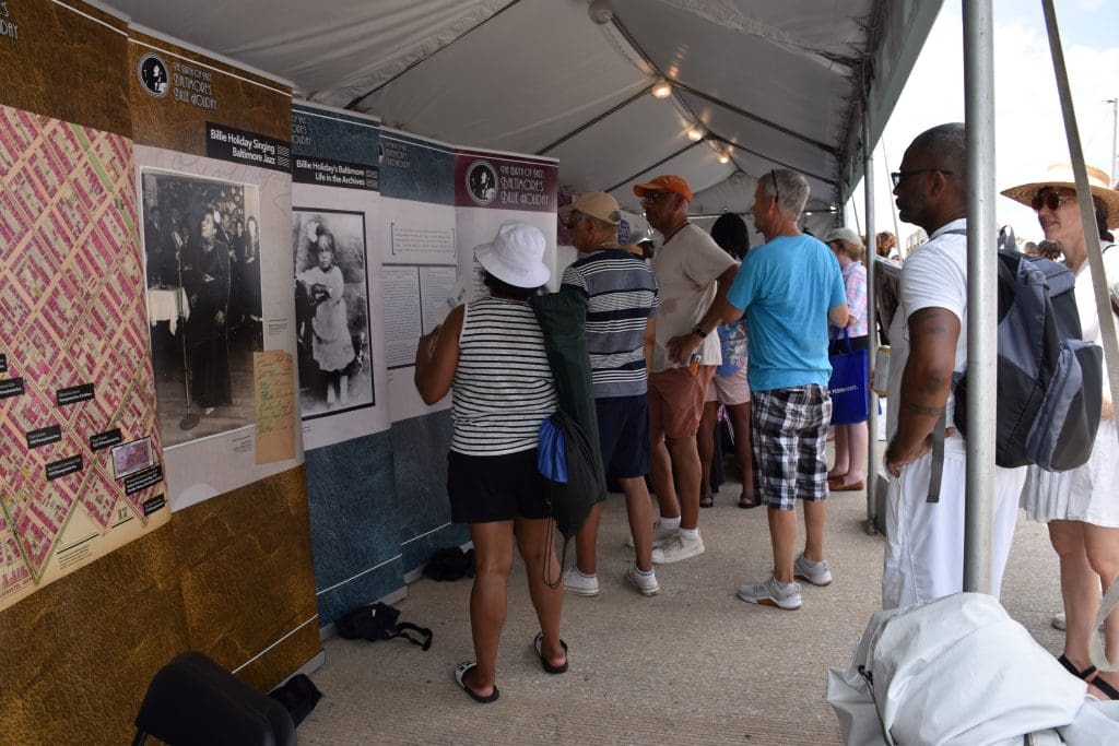A group of six people standing at the Billie Holiday banners and reading the material.