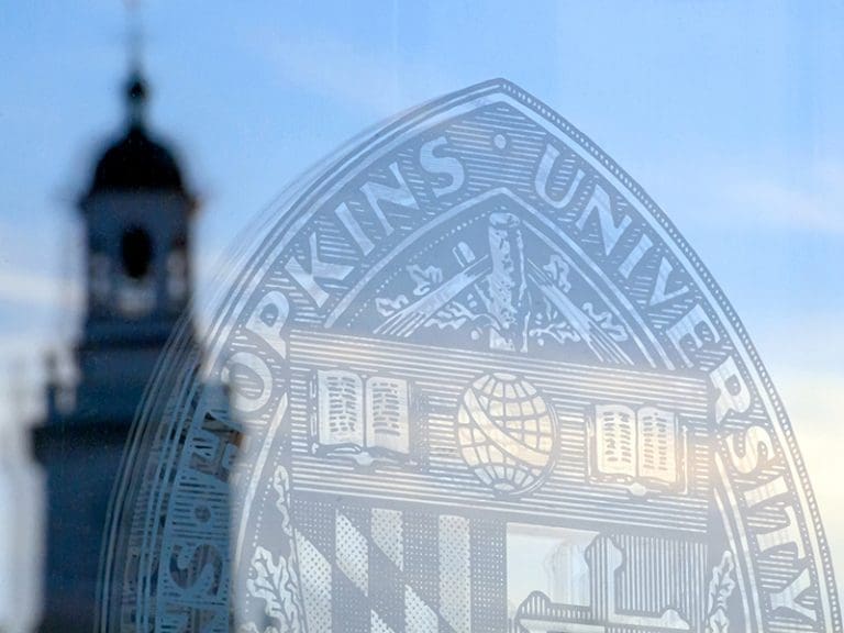 the johns hopkins shield engraved on glass with a tower in the background