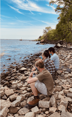 three people sitting on a rocky beach looking out at water
