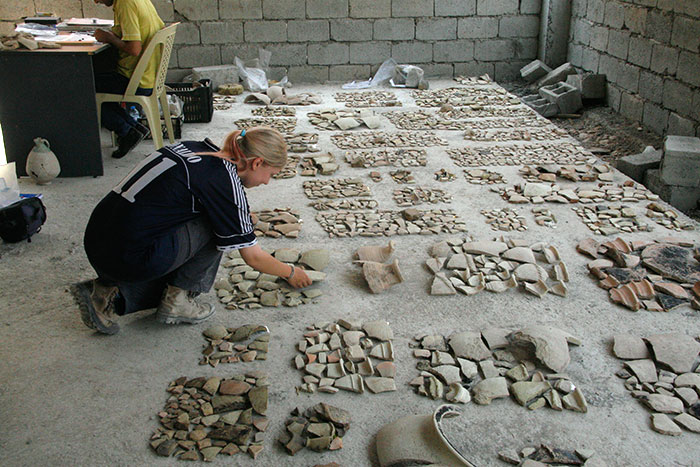 person sorting many pieces of broken tile and artifacts on the ground in rows