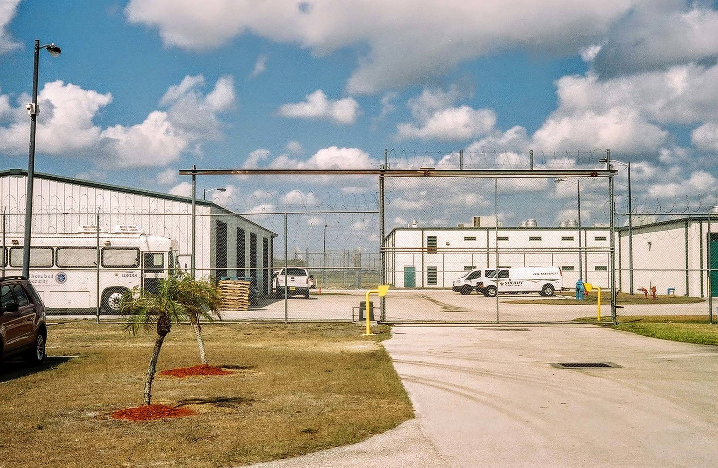 Jail parking area with tall fence and small palm trees