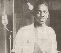 Young Black surgeon Vivien Thomas in apron with medical equipment behind him