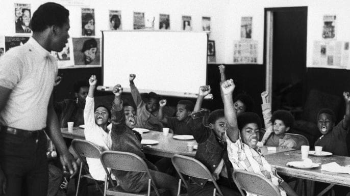 Black children sitting at table with fists raised in Black Panther Party class