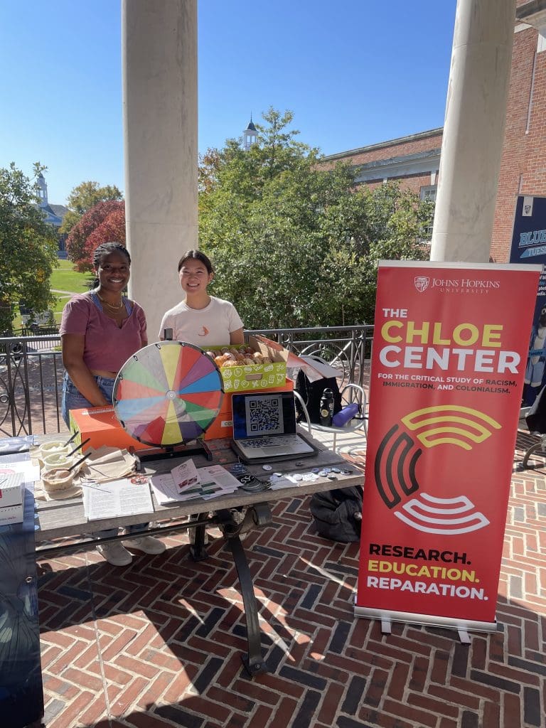 Two students stand at a table with the Chloe Center banner, handing out information about the CDS major